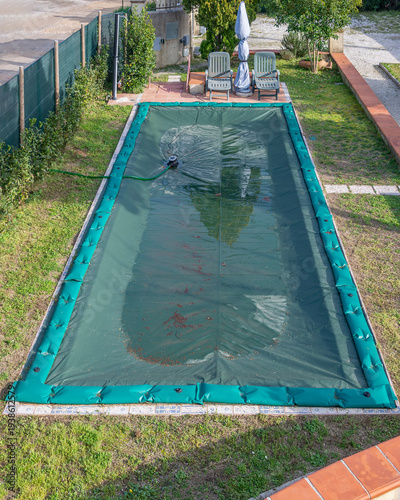Aerial view of a swimming pool that has been covered with a green tarp and tubes for the winter season