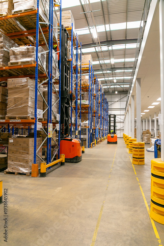 Canvas Print Modern industrial warehouse with narrow aisle pallet racking system and a forklift truck operating between shelves for storing and retrieving palletised goods