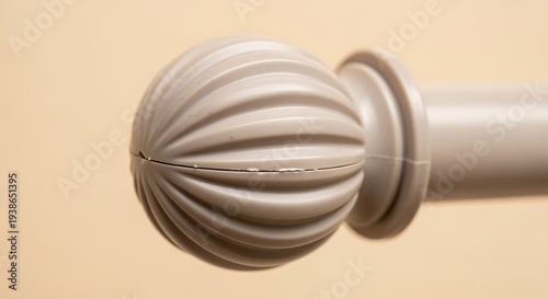 Closeup of a beige curtain rod finial and part of the rod on a beige background