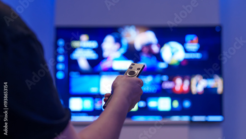 Hand holding remote control toward smart tv streaming screen