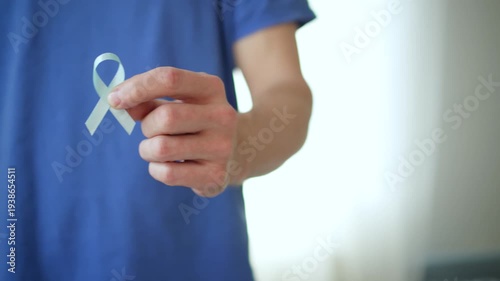 A man holds a blue satin ribbon in his hand, representing prostate cancer awareness, early detection, and support for patients and their families.