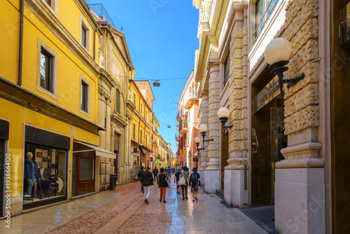 A narrow, colorful street of shops and sidewalk cafes in the historic old town of Verona, Italy.