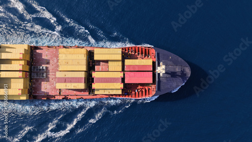 Aerial drone drone point of view photo above partial loaded container ship with colorful containers overlooking deep blue sea near logistics port