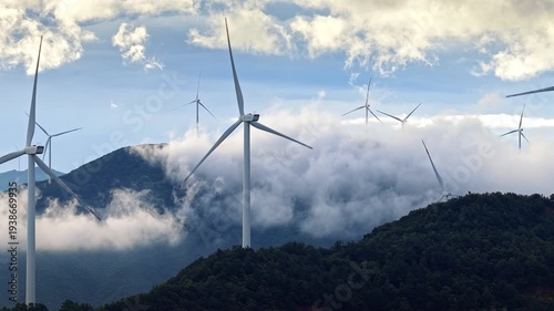 Wind turbines standing on mountain peaks above clouds at sunrise, generating renewable energy in Guilin, China.