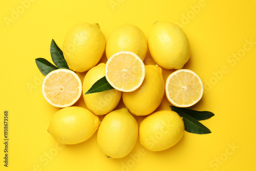 Ripe lemons and leaves on yellow background, flat lay