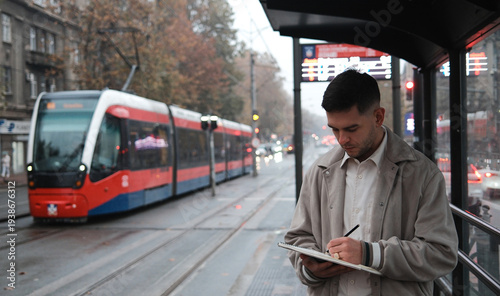 Cuadro en lienzo Young man writes in a notebook while waiting at a tram stop in the city