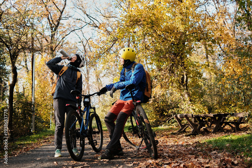 Woman drinking water while man rests on bicycle during autumn ride. Hydration and outdoor recreation concept.