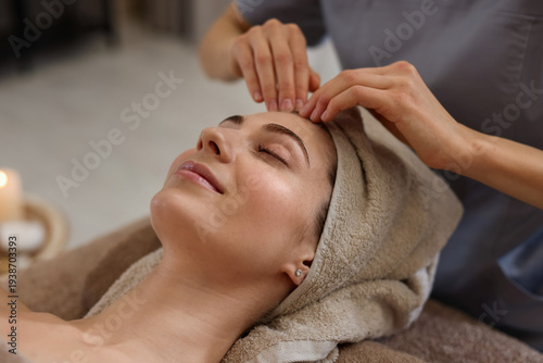Bild auf Leinwand Beautiful woman wrapped in towel receiving facial massage on couch indoors, clos
