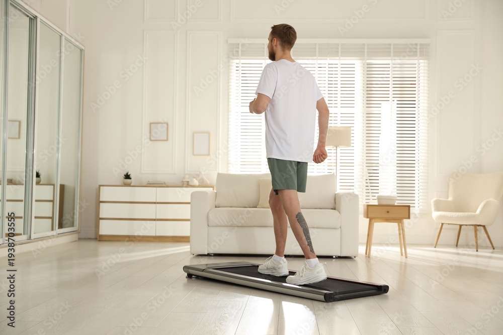 Fototapeta premium Sporty man training on treadmill at home, space for text