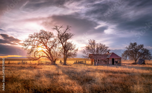Old abandoned wooden farmhouse on the prairie at sunset. Colorful clouds float silently in the sky. 
