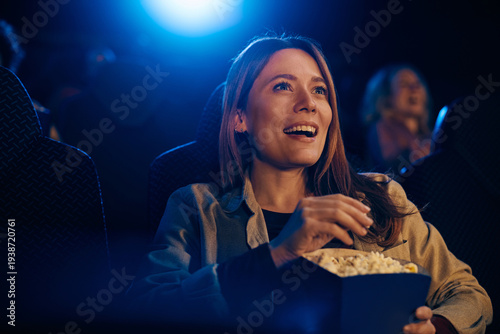 Happy woman eating popcorn during film screening in theater.