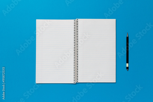 Open spiral notepad on a blue background. The page is blank and there is pen on the side.