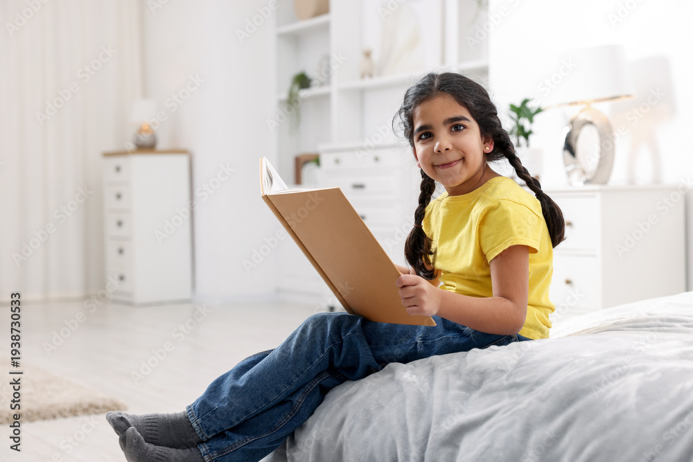 Naklejka premium Cute little girl reading book on bed at home