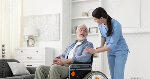 Care worker talking to senior man in wheelchair and moving away indoors