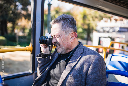 Fotografie Mature man photographing a city from a tour bus
