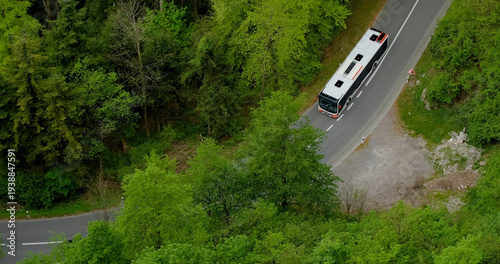Bus travels along winding road surrounded by green trees in a rural area during daytime