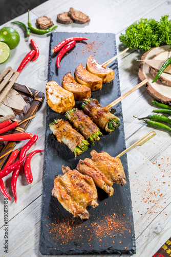 Grilled chicken wings and vegetable skewers seasoned with chili powder arranged on a slate board. The street style setup highlights spice and grilling suitable for barbecue and skewer concepts.