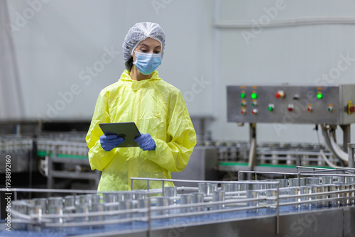 Clean room technician using tablet to inspect an automated production line in Canned food factory factory, highlighting quality control, hygiene standards, industrial safety, smart manufacturing.