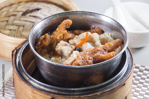 A metal bowl of steamed pork ribs in black bean sauce served over rice in a bamboo steamer basket.