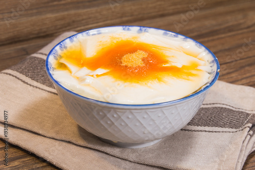 A white bowl of silky tofu pudding topped with golden syrup placed on a folded napkin