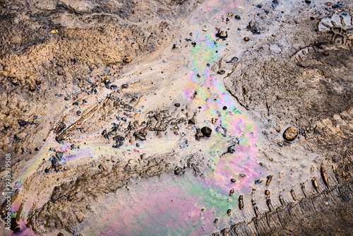 Colorful oil slick creating an iridescent pattern on wet mud and dirt, symbolizing environmental contamination and the impact of human activity