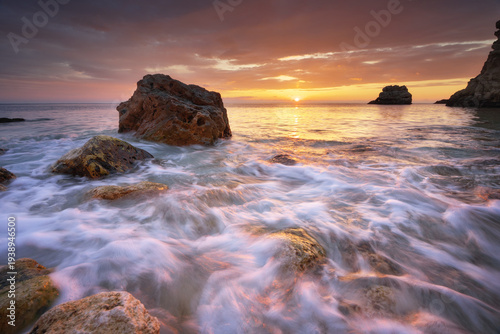 Dramatic sea sunset with fast flowing water over rocks and beautiful golden sunlight reflection.