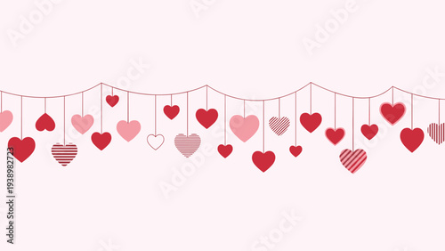 Decorative hanging heart garland with various red and pink hearts on strings against a soft light pink background.