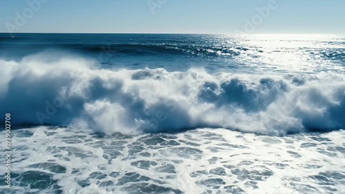 A crashing, translucent wave with frothy foam; clear sky. A bird is visible in the distance