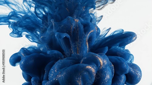 Abstract, vibrant blue ink and gold particles dispersing in liquid against a white backdrop