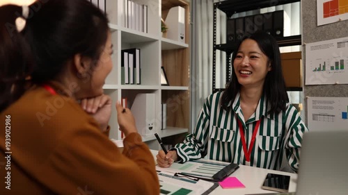 Two businesswomen discussing startup ideas and reviewing documents during a meeting in modern office, representing teamwork, business planning and collaboration in a startup company.