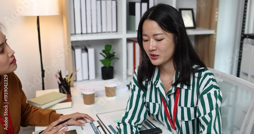 Two businesswomen discussing startup ideas and reviewing documents during a meeting in modern office, representing teamwork, business planning and collaboration in a startup company.