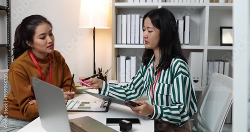 Two businesswomen discussing startup ideas and reviewing documents during a meeting in modern office, representing teamwork, business planning and collaboration in a startup company.