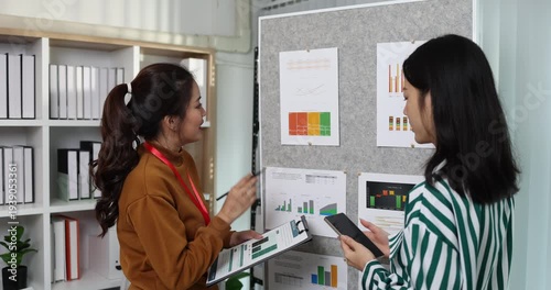 Two businesswomen discussing startup ideas and reviewing documents during a meeting in modern office, representing teamwork, business planning and collaboration in a startup company.