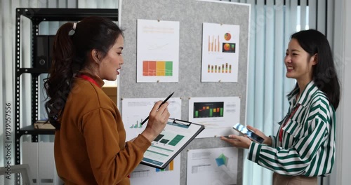 Two businesswomen discussing startup ideas and reviewing documents during a meeting in modern office, representing teamwork, business planning and collaboration in a startup company.