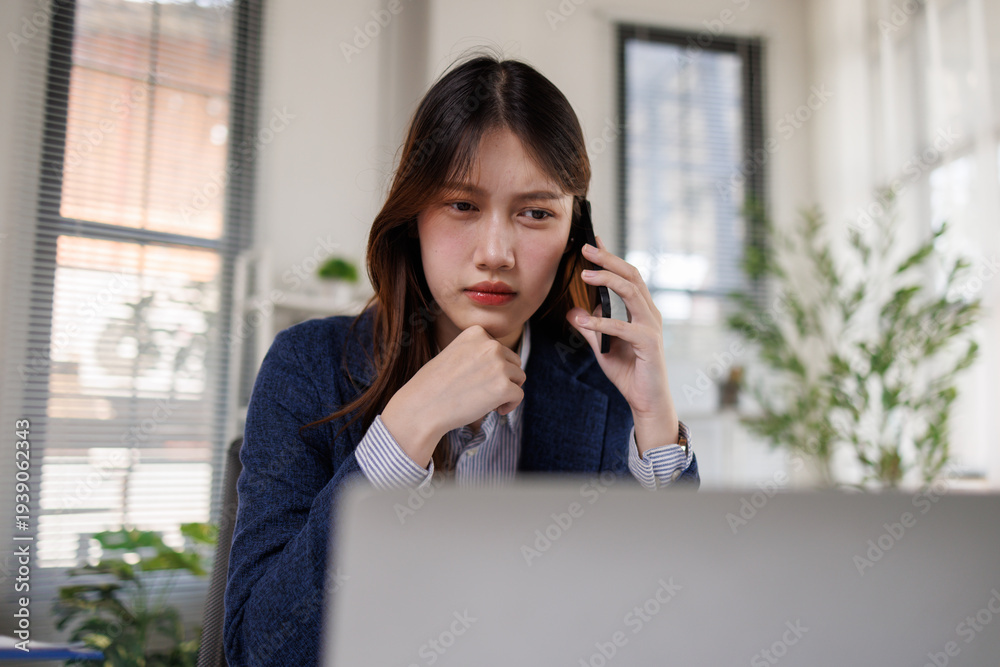 Obraz premium Confident Asian businesswoman talking on smartphone and smiling at office desk