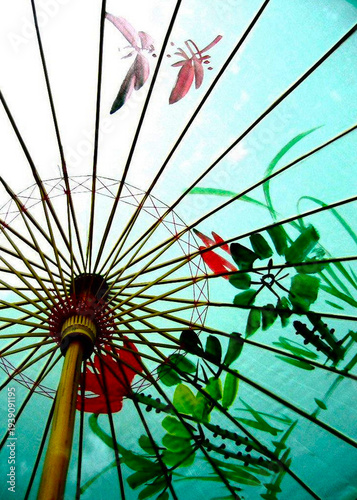 a colorful umbrella with red flowers and green leaves on a sunny day with dragonflies flying overhea