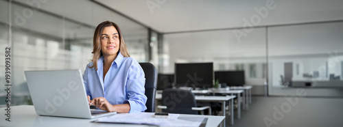 Fotografie Happy mature middle aged professional business woman bank worker or hr manager, corporate executive looking away at work working on laptop computer in office thinking of business technology future
