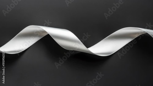White ribbon curves gracefully against dark background. Soft lighting highlights its smooth, flowing texture. Simple composition draws attention to ribbon's elegant shape