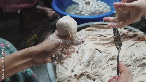 Hands shaping a meatball from a mixture, with a large bowl of pre-formed meatballs in the background.