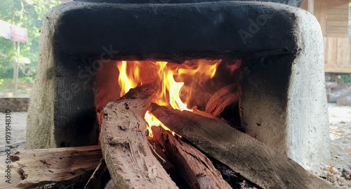 A traditional cement stove with a fire burning inside, fueled by logs of wood, and emitting wisps of smoke.