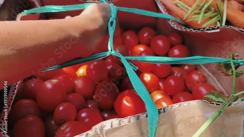 A hand reaches into a cardboard box filled with ripe red tomatoes. 