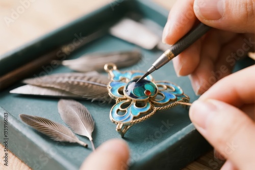 Close-up of hands crafting an ornate enamel jewelry piece with fine tools and feathers nearby