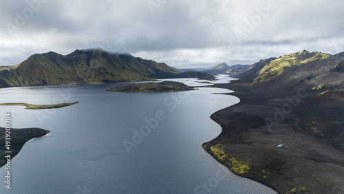 Aerial view on huge volcanic lake with approaching tiny cars and mountains in backdrop, Iceland