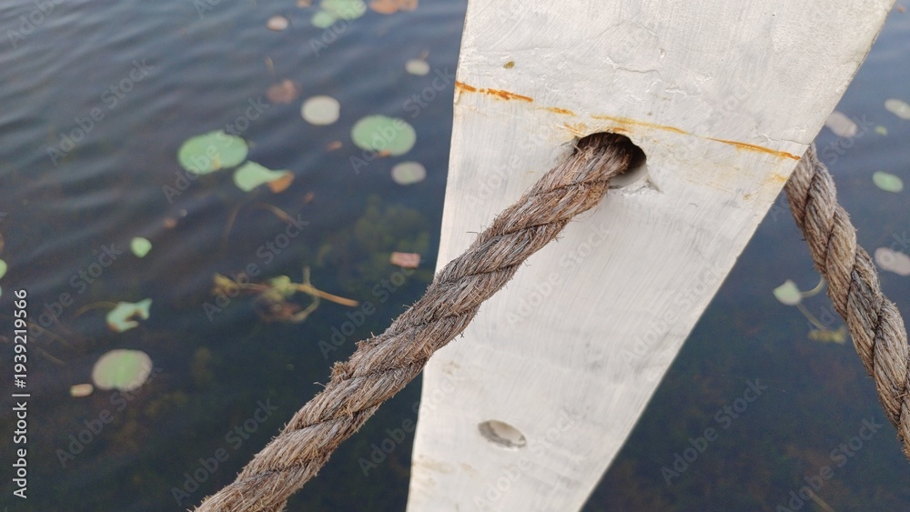 Naklejka premium Thick rope passing through a white wooden bridge post over a lake
