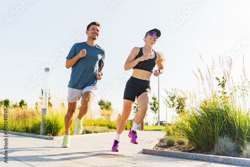 Healthy man and woman jogging together on a sunny urban park path in athletic wear during daytime