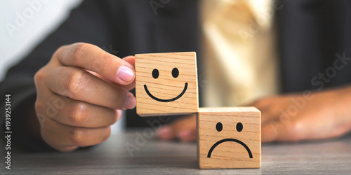Mental health care concept and training in emotional control with a hand placing a smiling wooden block on top of a sad faced block