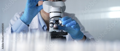 Canvastavla Woman scientist wearing lab coat, white protective gloves and glasses, is using microscope in modern laboratory setup, portrait view
