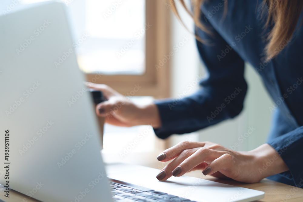 Fototapeta premium Close up of business woman working on laptop, surfing the net and holding a cup of coffee at office, corporate business concept