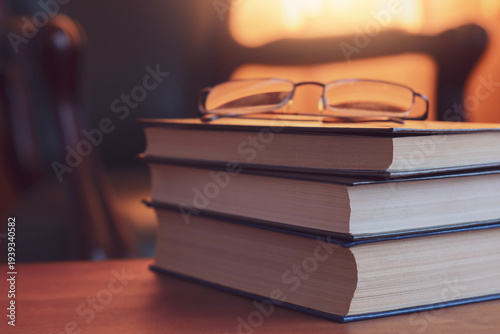 Cozy reading atmosphere with stack of books and eyeglasses on wooden table in warm evening light
