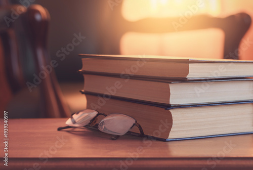 Cozy reading atmosphere with stack of books and eyeglasses on wooden table in warm evening light